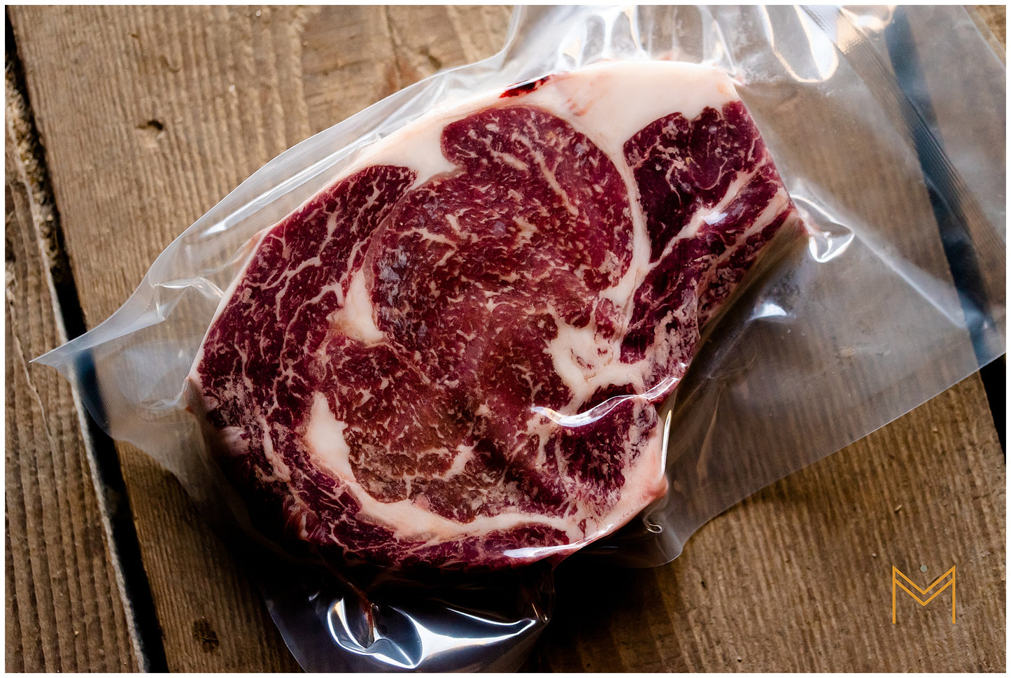 A vacuum-sealed package containing a bone-in ribeye steak displayed on a wooden surface.