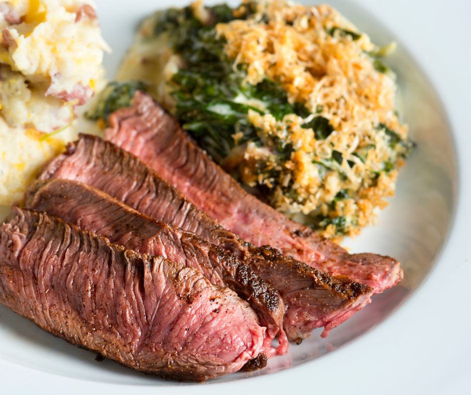 A plate containing slices of London Broil beef, mashed potatoes, and a breaded vegetable.