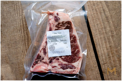 A packaged T-Bone steak with visible marbling, placed on a wooden surface.